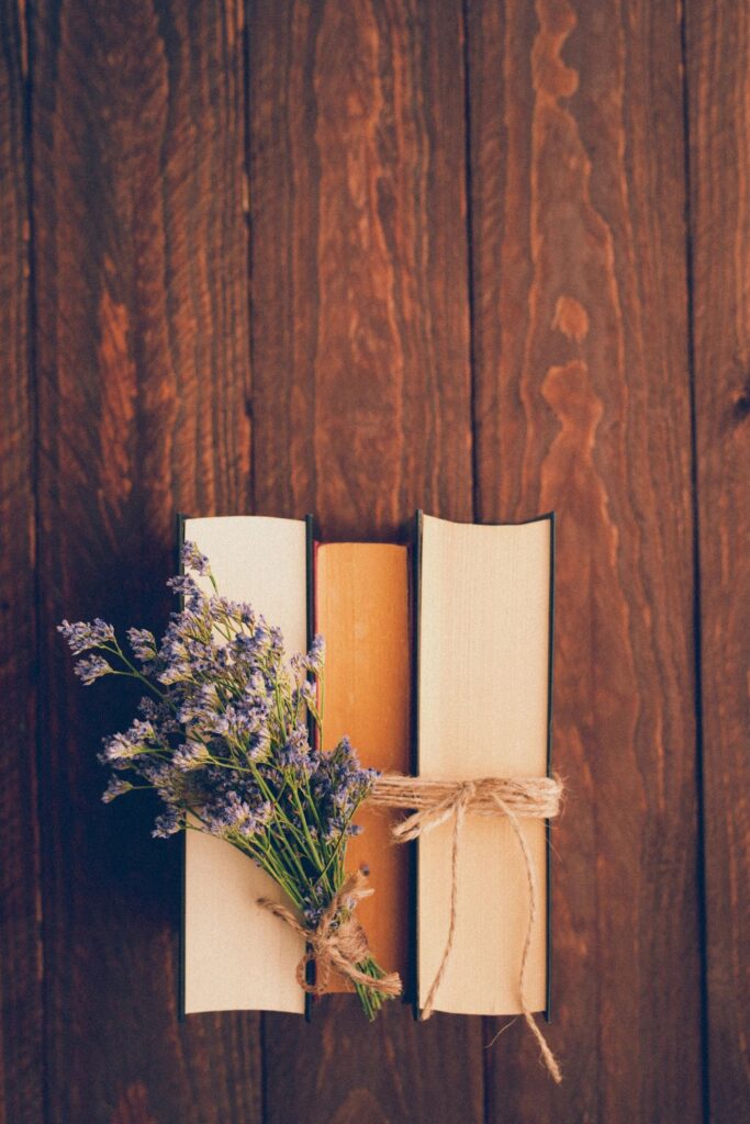 Top view of a beautiful flat lay in retro style with laced old vintage books in a row and a little lilac flower bouquet on dark wooden background and copy space on the top