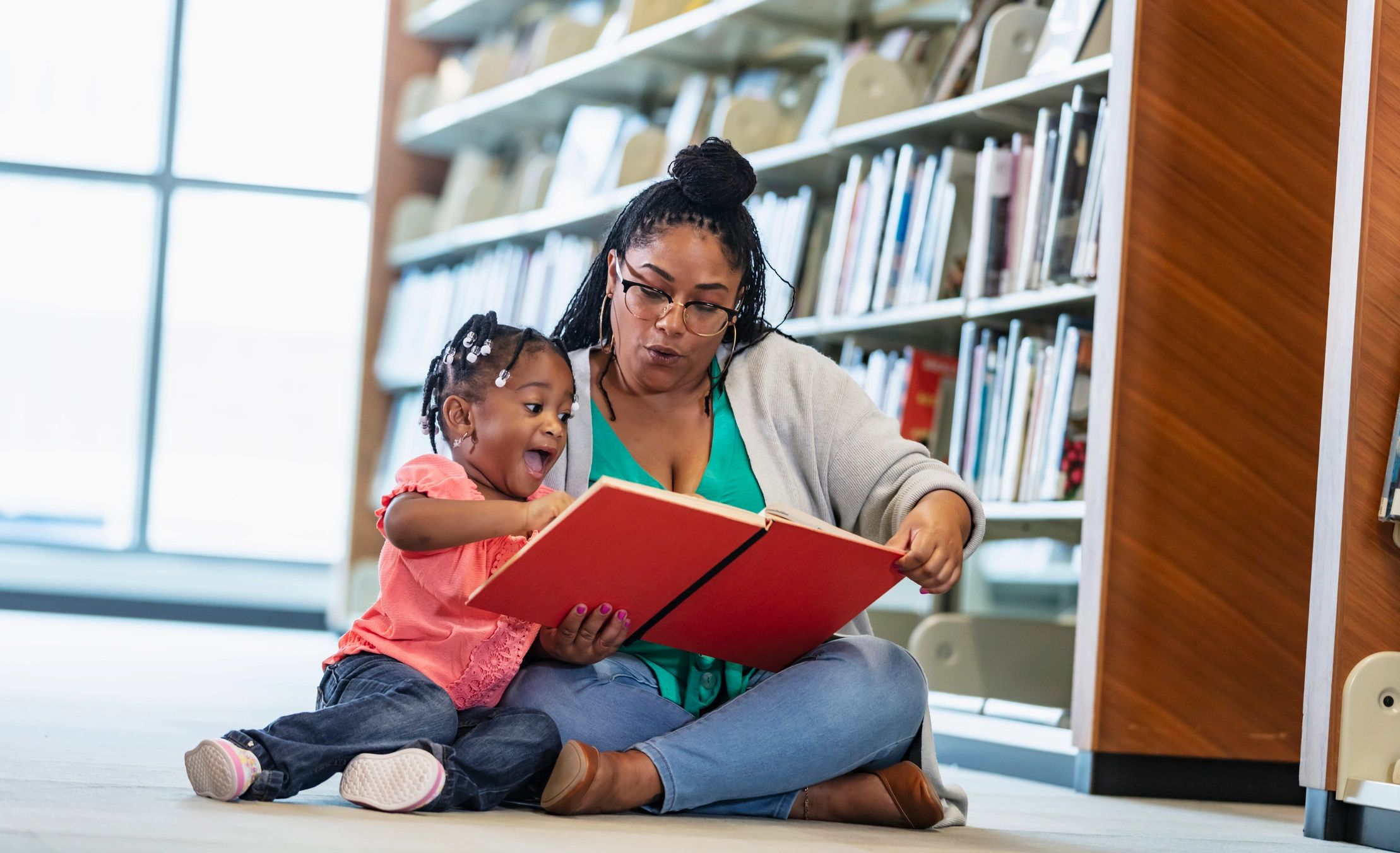 Excited little girl reading with her mother in a library